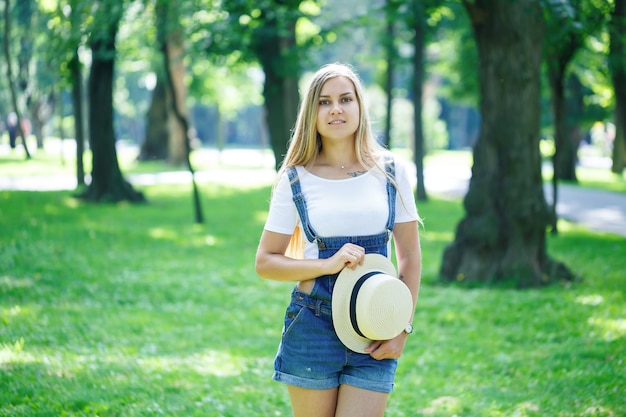 KYIV, UCRAINA - Agosto 2019 giovane bella ragazza in tuta di jeans e un cappello leggero che cammina nel parco