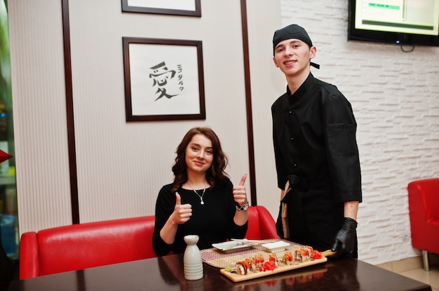 L'abbigliamento da chef professionale in nero offre sushi e panini per cliente donna in un ristorante di cibo tradizionale giapponese.