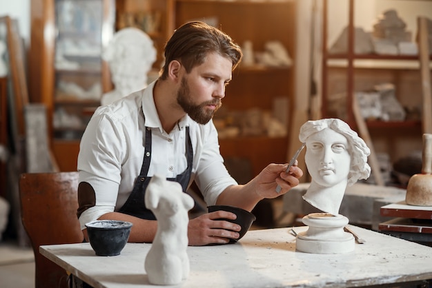 L'abile scultore esegue un restauro professionale della scultura in gesso della testa della donna nel laboratorio creativo.