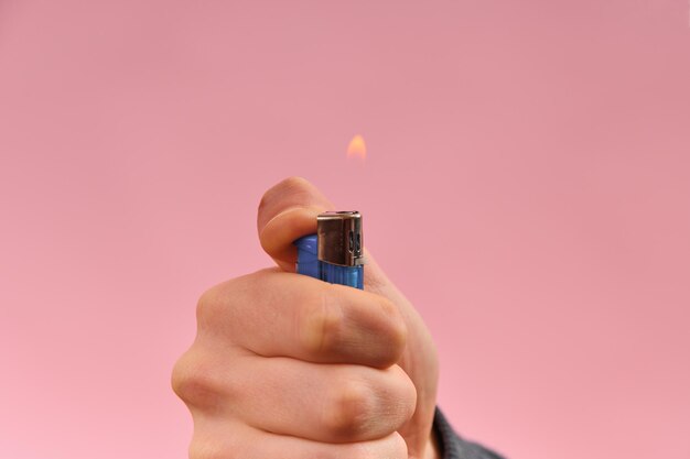 L'accendino in fiamme nella mano di un uomo su uno sfondo rosa