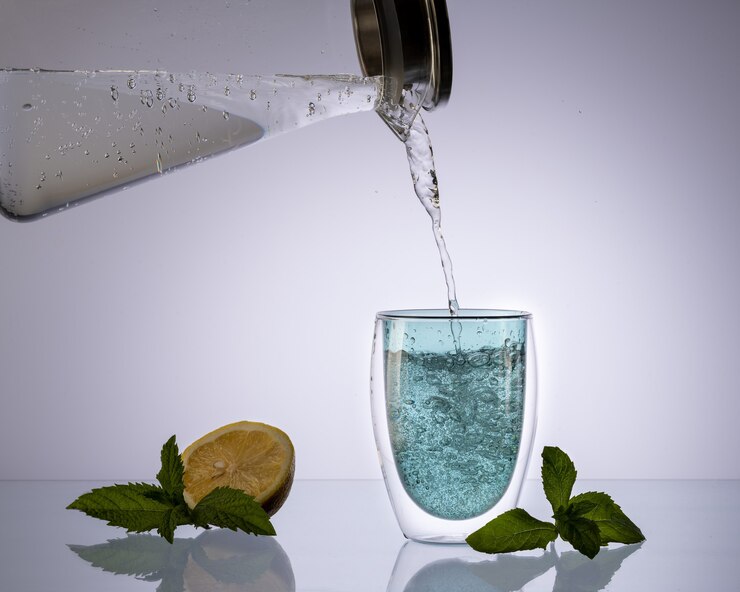 L'acqua che versa nel vetro dal decanter di vetro su sfondo azzurro trasparente, beve acqua pulita, concetto.