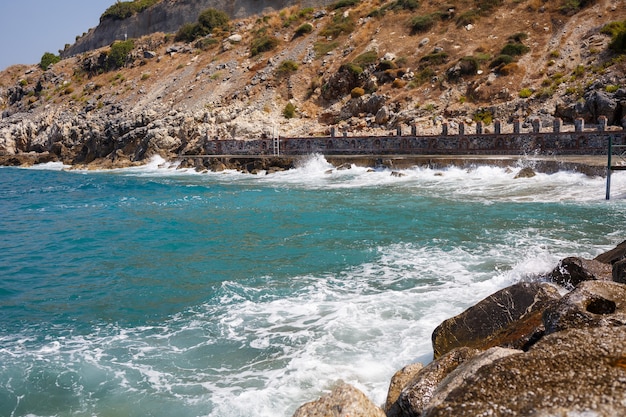 L'acqua di mare batte contro le rocce rocciose e fa le onde con la schiuma, molo robusto nel mare