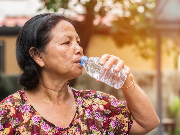 L&#39;acqua potabile della donna asiatica anziana dalla bottiglia