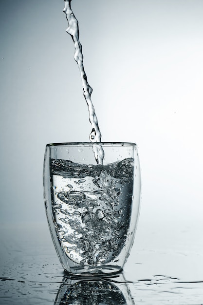 L'acqua pura fresca e fredda viene versata in un bicchiere. Acqua purificata in un bicchiere su una parete grigia. Spruzzata di congelamento del movimento di acqua cristallina sulla parete grigia.