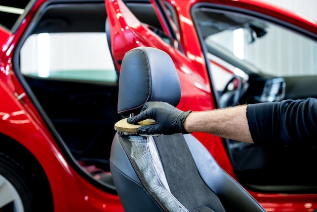 L'addetto al servizio auto pulisce un seggiolino auto con una spazzola speciale