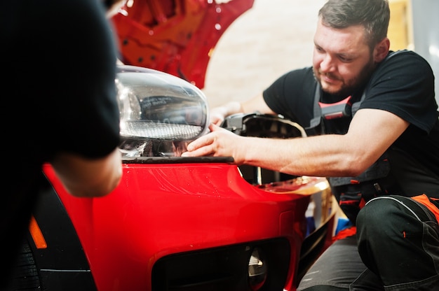 L'addetto all'assistenza automobilistica ha messo una pellicola antighiaia su una carrozzeria rossa presso l'officina del veicolo di dettaglio