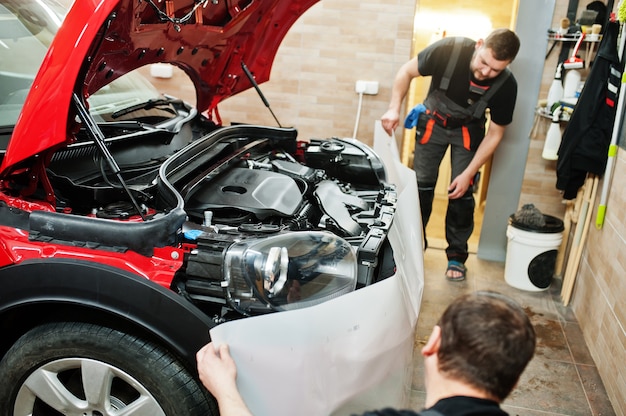 L'addetto all'assistenza automobilistica ha messo una pellicola antighiaia su una carrozzeria rossa presso l'officina del veicolo di dettaglio