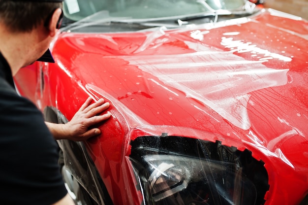 L'addetto all'assistenza automobilistica ha messo una pellicola antighiaia su una carrozzeria rossa presso l'officina del veicolo di dettaglio