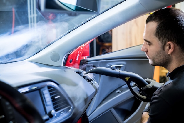 L'addetto alla manutenzione dell'auto pulisce gli interni con un pulitore a vapore