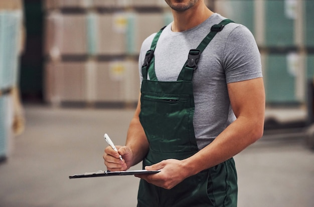 L'addetto allo stoccaggio in uniforme di colore verde e il blocco note in mano controlla la produzione.