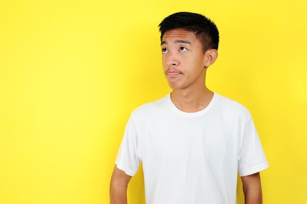 L'adolescente bello guarda lo spazio della copia con una t-shirt bianca, isolata su sfondo giallo