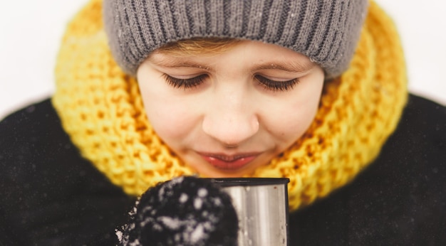 L'adolescente beve il tè caldo nella foresta di inverno.