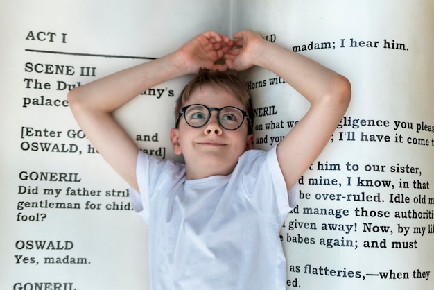 L'adolescente con gli occhiali si trova su un libro enorme Il bambino bibliofilo ama leggere la letteratura nel concetto di scuola L'amore nei libri