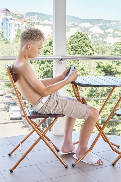 L'adolescente con il torso nudo legge l'ebook con l'espressione seria del viso seduto sul balcone dell'hotel