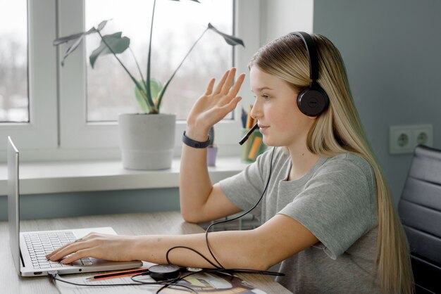 L'adolescente in cuffia alza la mano mentre tiene lezione online a casa