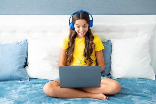 L'adolescente in cuffia si rilassa a letto a casa ascolta la musica utilizzando il laptop Child in earphones