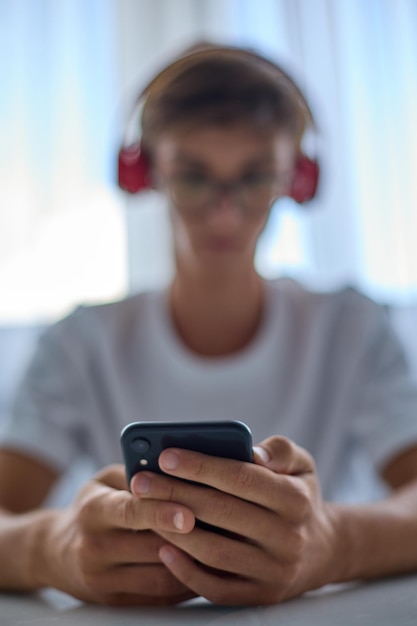 L'adolescente moderno in cuffia e una maglietta bianca guarda il telefono