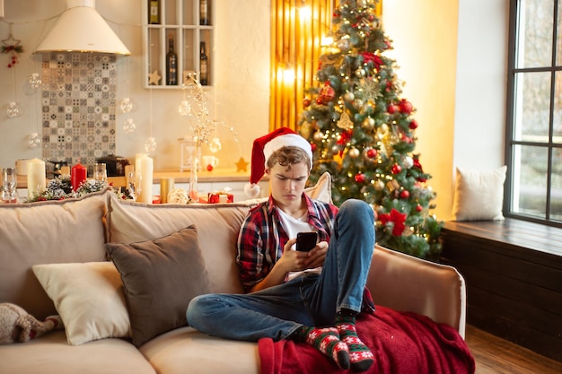 L'adolescente si siede sul divano indossando un cappello da Babbo Natale e con un telefono in mano comunicazione online