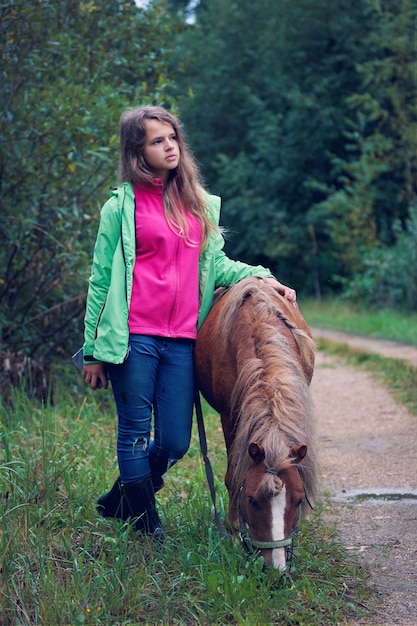 L'adolescente sta con un piccolo cavallo sul ciglio della strada del paese nella sera d'estate piovosa