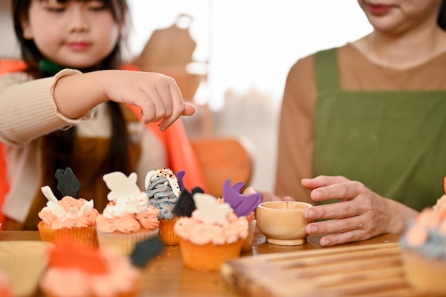 L'adorabile bambina asiatica e sua madre si divertono a decorare insieme i cupcakes di Halloween