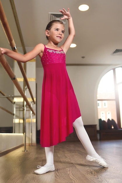 L'affascinante bambina sogna di diventare una ballerina La ragazza con l'abito rosa balla aggrappandosi al barLa bambina studia danza classica