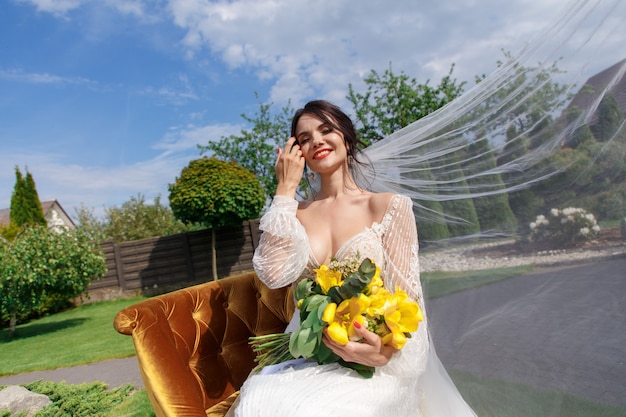 L'affascinante sposa tiene un bouquet da sposa e si siede nel cortile