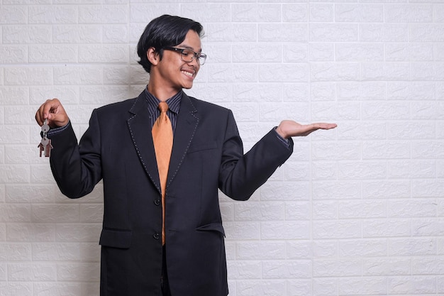 L'agente immobiliare sorridente che indossa la tuta tiene la chiave di casa e gesturing la mano mostrando o presentando