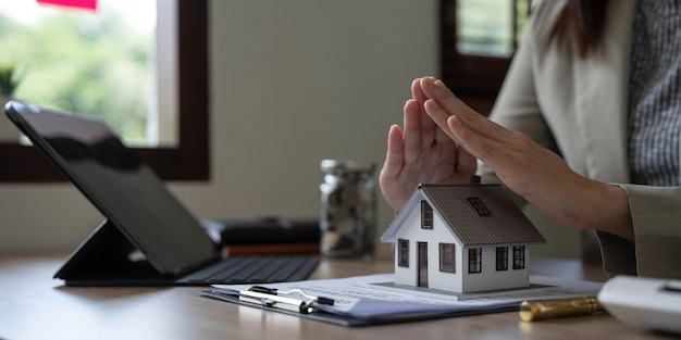 L'agente immobiliare usa le mani per proteggere i tetti rossi il concetto di proteggere le case usando i gesti e i simboli degli investitori immobiliari che si prendono cura del credito e dei contratti