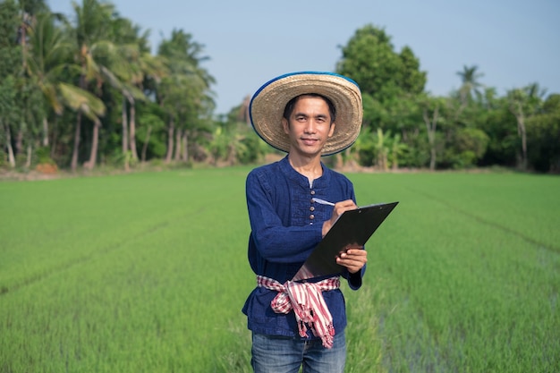 L'agricoltore asiatico indossa il costume tradizionale in piedi e scrive su un cartone al verde