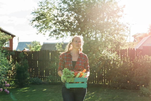 L'agricoltore femminile che trasporta una scatola di verdure raccolte copia lo spazio giardino e raccoglie prodotti agricoli per la vendita online