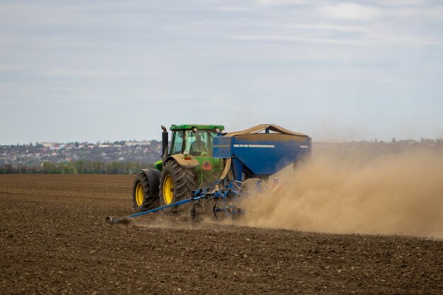 L'agricoltore in trattore che prepara la terra con il coltivatore del semenzaio come parte delle attività pre semina all'inizio della primavera di lavori agricoli ai terreni agricoli