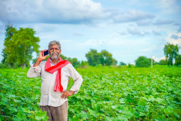 L'agricoltore indiano parlando al telefono cellulare al campo agricolo