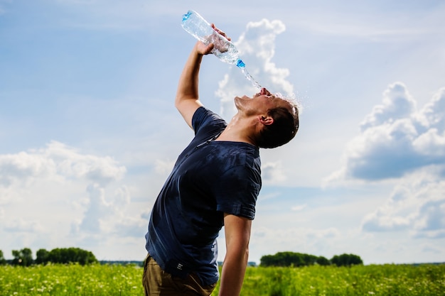 L'agricoltore stanco e assetato sta bevendo acqua nel campo durante la pausa dall'attività agricola