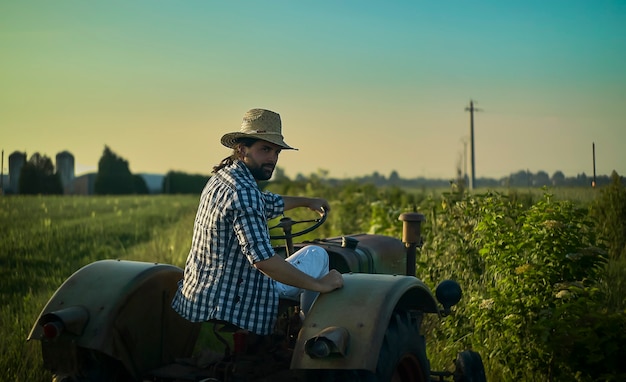 L'agricoltore sul trattore lavora nei campi al tramonto