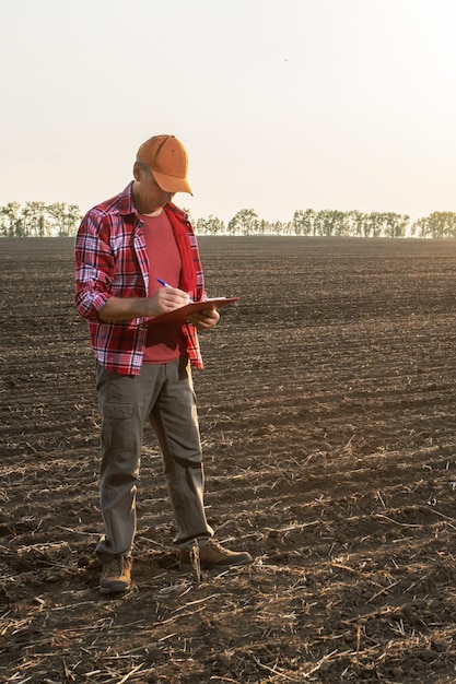 L'agricoltore uomo in piedi in campo usa la lista di controllo sulla lavagna per appunti per controllare la qualità del lavoro agricolo