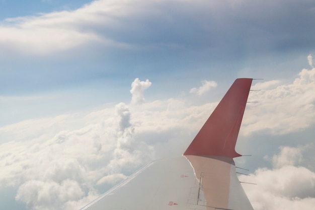 L'ala rossa di un aeroplano nel cielo blu. Nuvole e cielo visibili attraverso l'oblò. Concept - voliamo a riposare