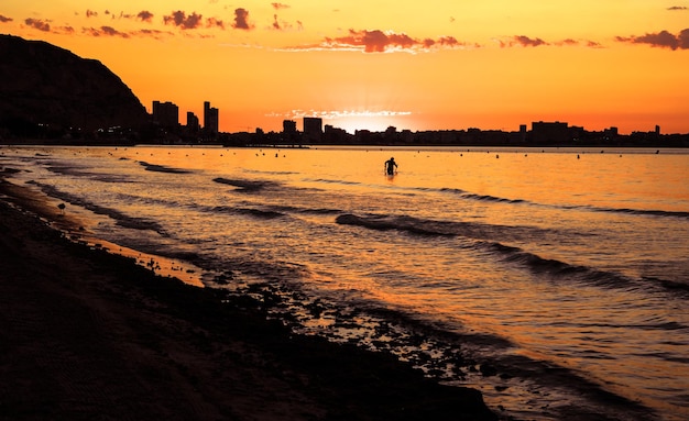 L'alba vista dalla spiaggia di postiguet ad Alicante, con edifici e persone in controluce.