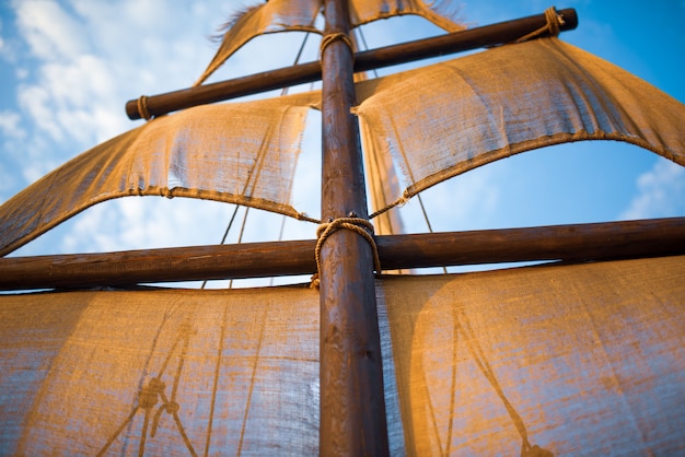 L'albero della nave con le vele beige oscilla contro un cielo blu