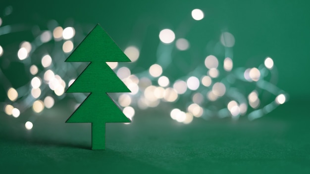 L'albero di Natale verde in legno si erge sullo sfondo delle luci della ghirlanda, su uno sfondo verde. Tema natalizio. Giocattoli per bambini.