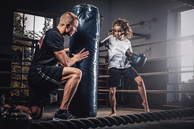 L'allenatore di pugili esperto sta allenando la nuova pugile bambina per competizioni speciali usando il sacco da boxe.