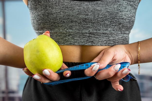 L'allenatore tiene in mano una mela verde e un nastro di misurazione per misurare il corpo è avvolto in mano Concetto di stile di vita sano