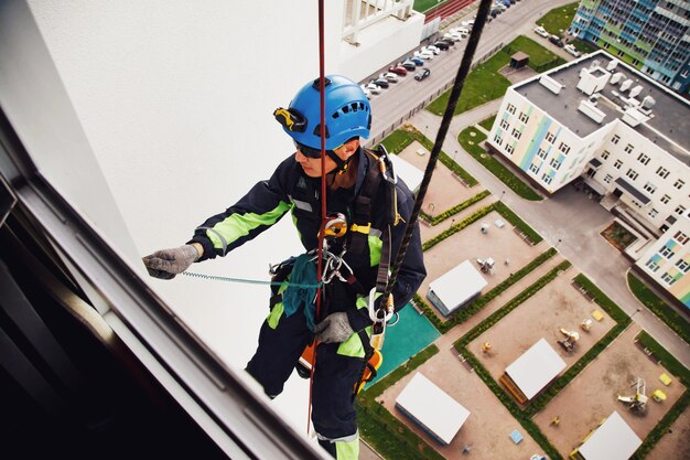 L'alpinista industriale pende dall'edificio residenziale mentre lava i vetri della facciata esterna. L'addetto alla fune è appeso al muro della casa. Concetto di opere urbane. Copia spazio