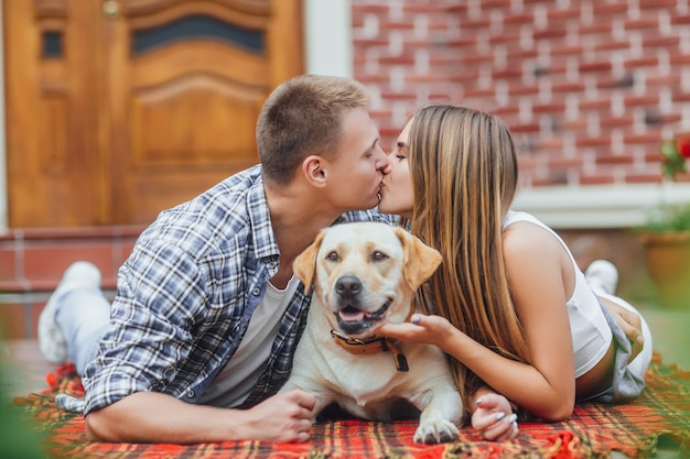 L'amore è tutto. Coppie sorridenti felici che riposano al cortile con un cane. Giovane famiglia sdraiata sul tappeto coperta e baciare.