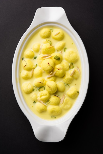 L'Angoori Rasmalai è un dessert indiano dolce con frutta secca e condimenti allo zafferano, servito in una ciotola su uno sfondo lunatico. messa a fuoco selettiva