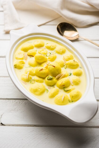 L'Angoori Rasmalai è un dessert indiano dolce con frutta secca e condimenti allo zafferano, servito in una ciotola su uno sfondo lunatico. messa a fuoco selettiva