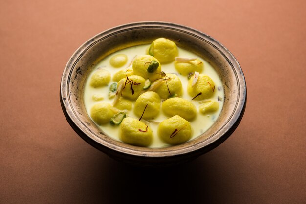 L'Angoori Rasmalai è un dessert indiano dolce con frutta secca e condimenti allo zafferano, servito in una ciotola su uno sfondo lunatico. messa a fuoco selettiva