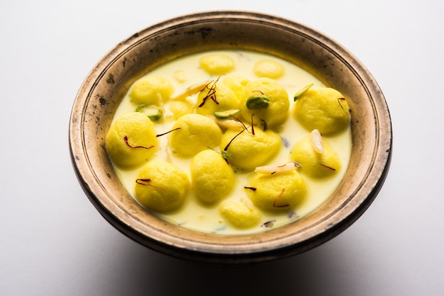 L'Angoori Rasmalai è un dessert indiano dolce con frutta secca e condimenti allo zafferano, servito in una ciotola su uno sfondo lunatico. messa a fuoco selettiva