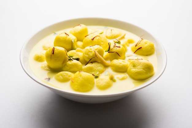 L'Angoori Rasmalai è un dessert indiano dolce con frutta secca e condimenti allo zafferano, servito in una ciotola su uno sfondo lunatico. messa a fuoco selettiva