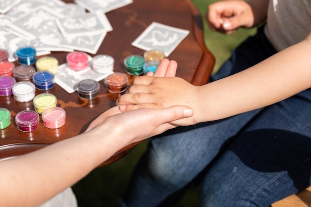 L'animatore per bambini sta creando un tatuaggio luccicante scintillante sulla mano di un bambino a una festa di compleanno