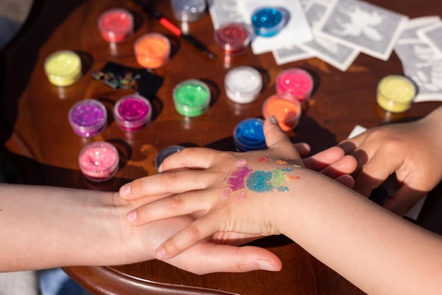 L'animatore per bambini sta creando un tatuaggio luccicante scintillante sulla mano di un bambino a una festa di compleanno